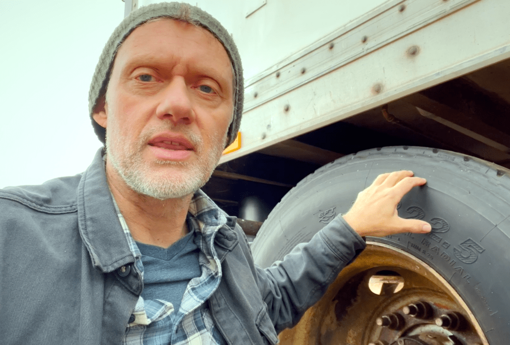 A person inspecting the tire of a semi-trailer, highlighting its size and condition.